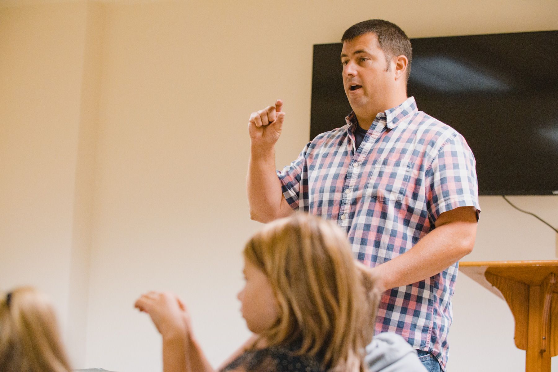 Man gestures while speaking to unseen children in a light-colored room.
