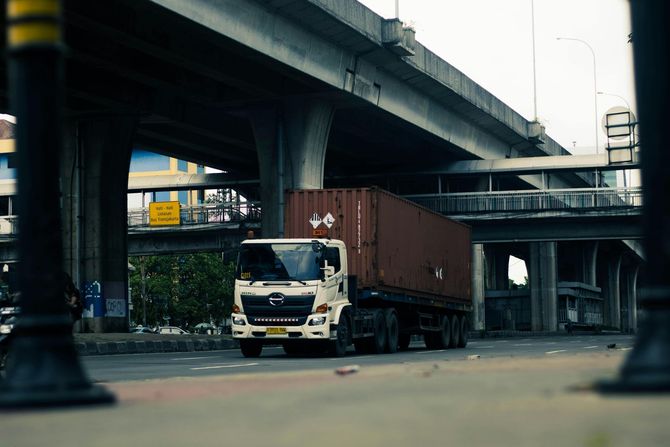Garbage truck workers collecting trash from a yellow bin. One worker stands, the other works in the truck.