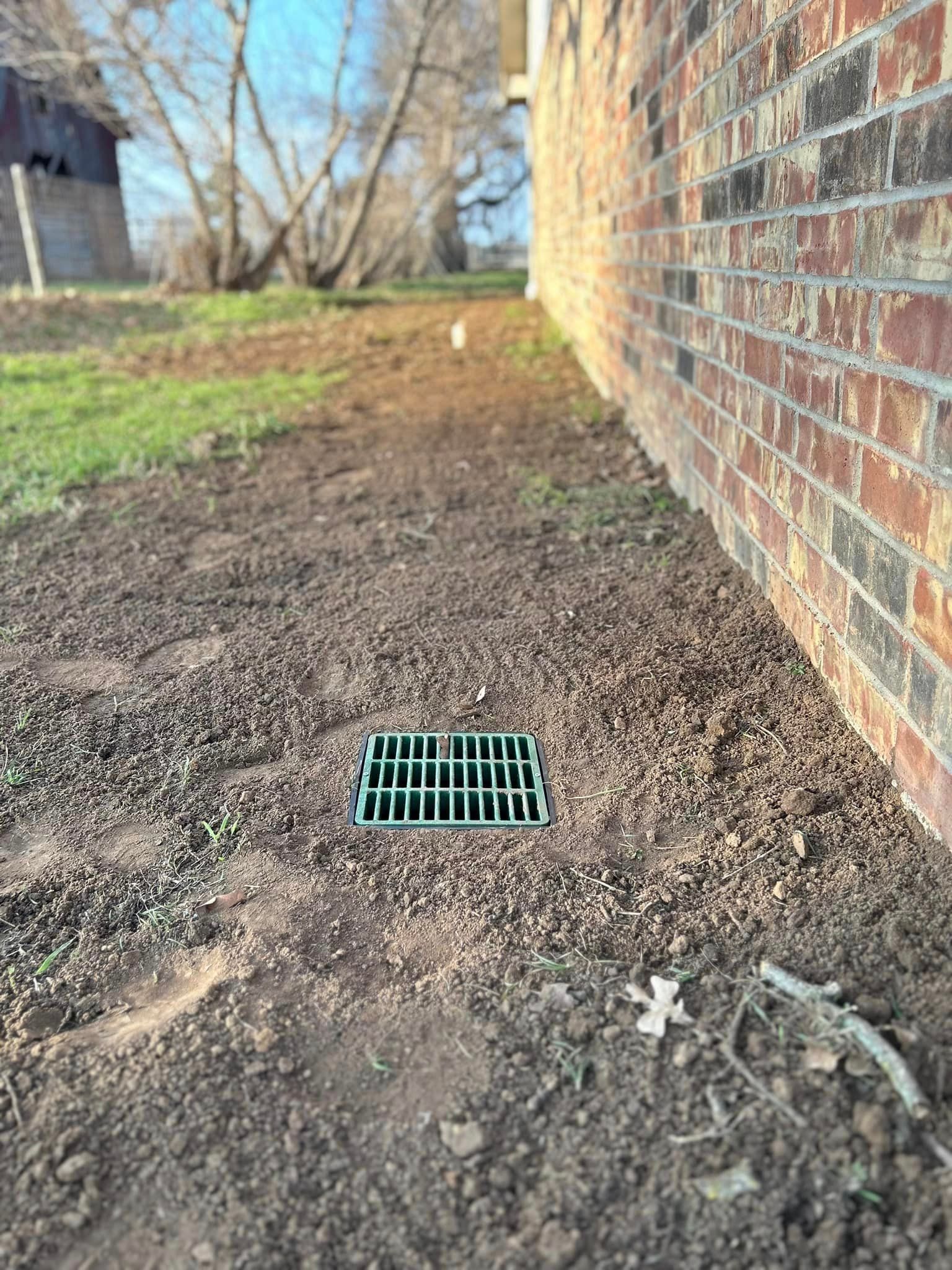 A Green Drain Is Sitting in The Dirt Next to A Brick Wall - Collinsville, TX - L5 Irrigation
