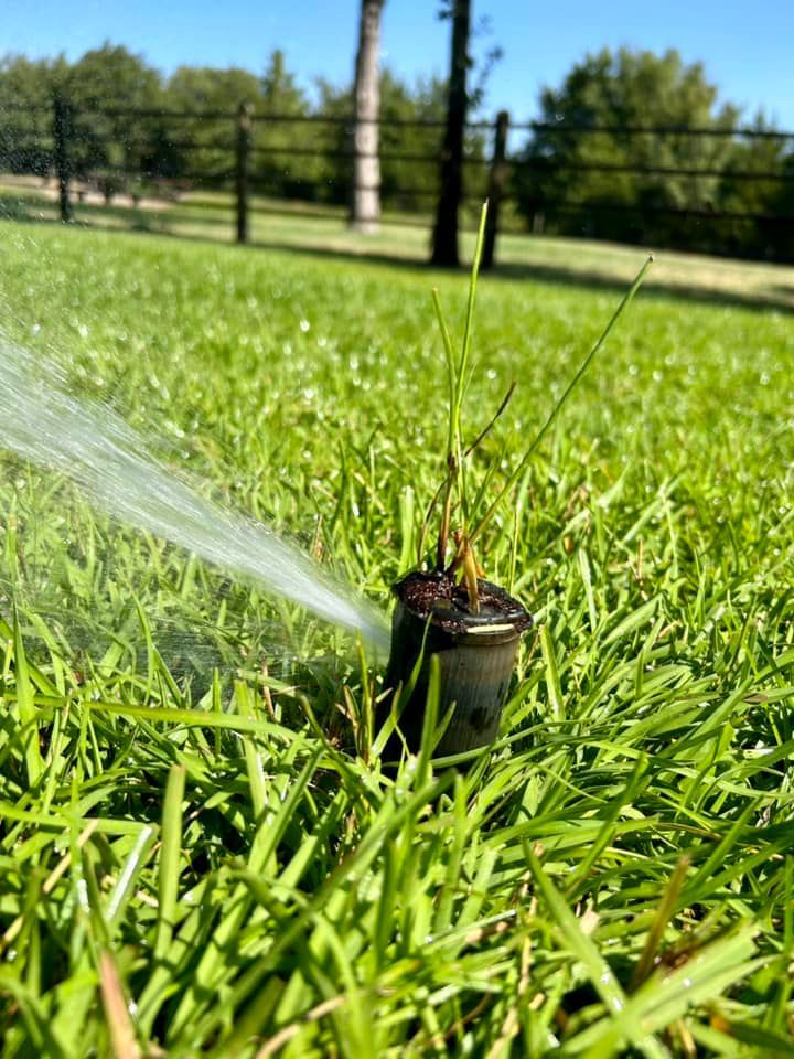 A Sprinkler Is Spraying Water on A Lush Green Field in Front of A Stone Building - Collinsville, TX - L5 Irrigation