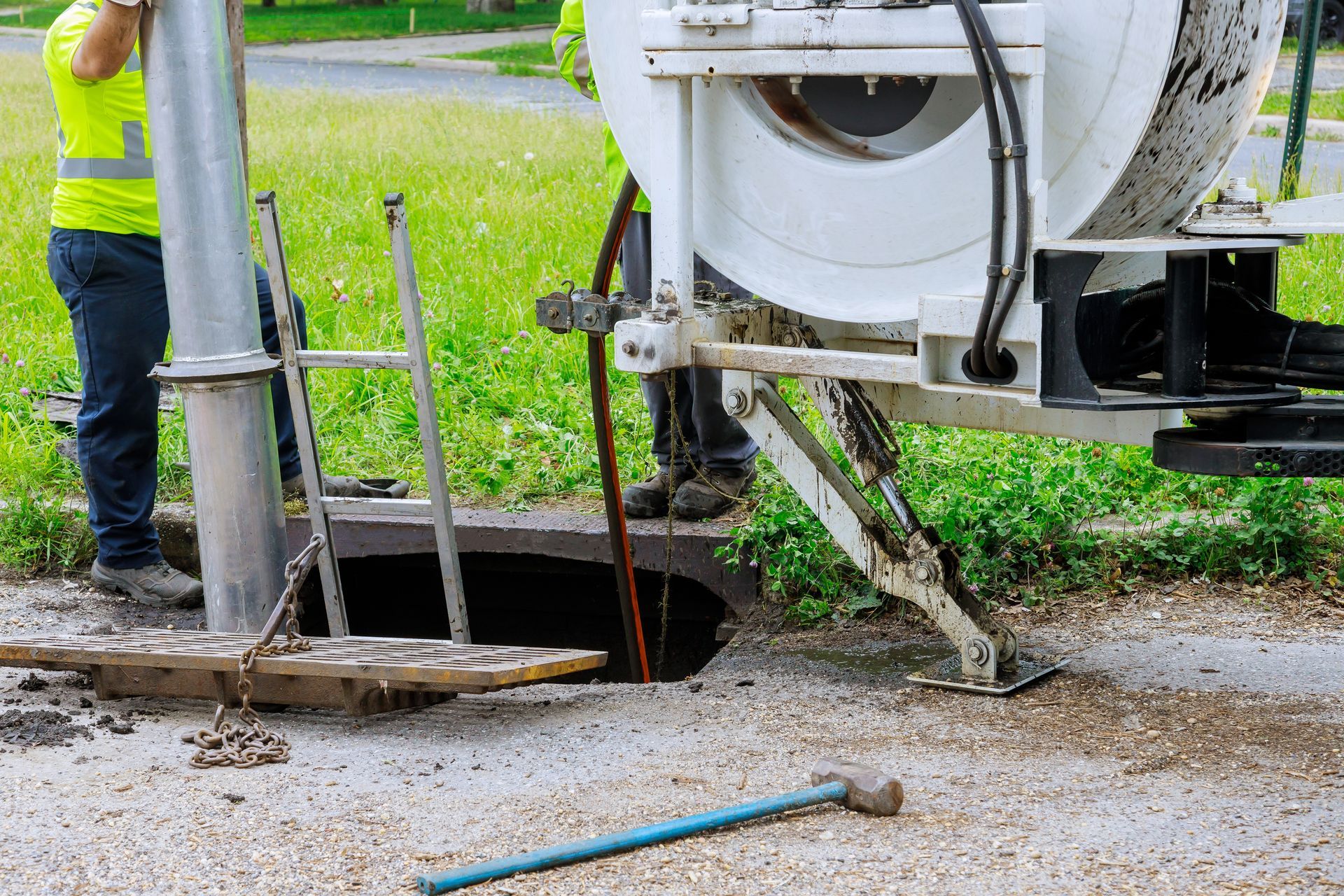Workers with a large machine are cleaning a sewer drain in a street.