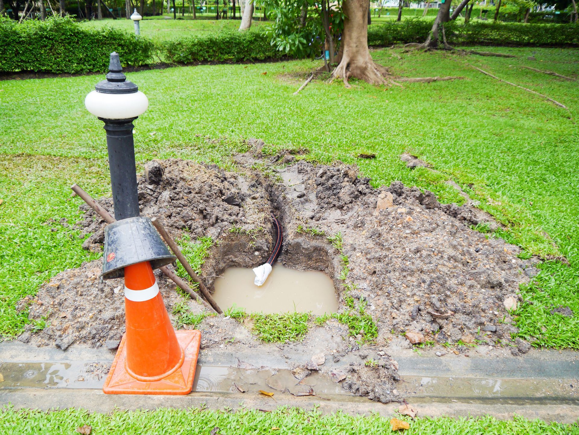 A cone is sitting in the middle of a hole in the ground in a park.