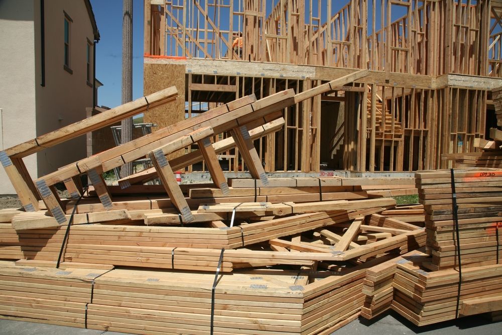 A pile of wood sits in front of a house under construction