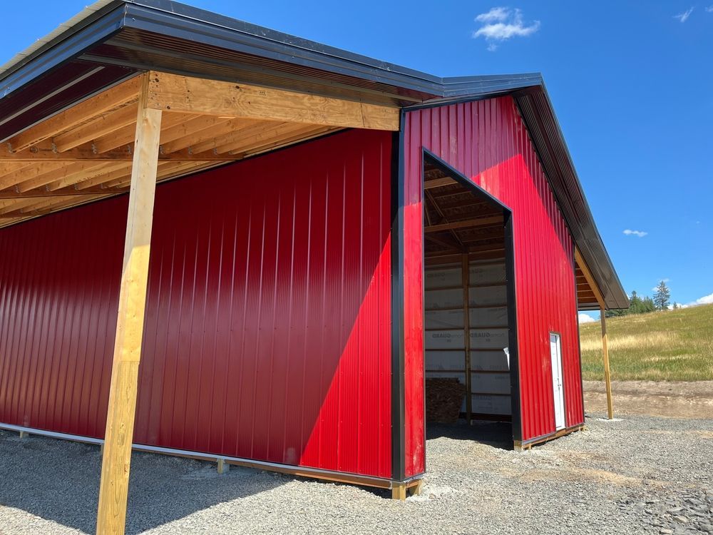 A red barn with a wooden roof is sitting on top of a gravel field.