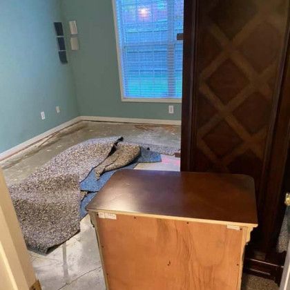Room with removed carpet, blue walls, wooden furniture, and a window.