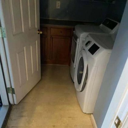 Laundry room with white washer and dryer, wood cabinets, and a partially open white door.