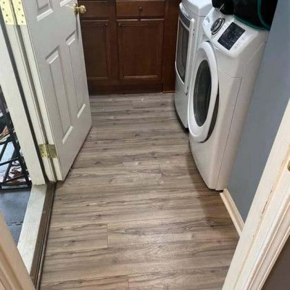 Laundry room with wood-look flooring, washing machine, dryer, cabinets, and a partially open door.