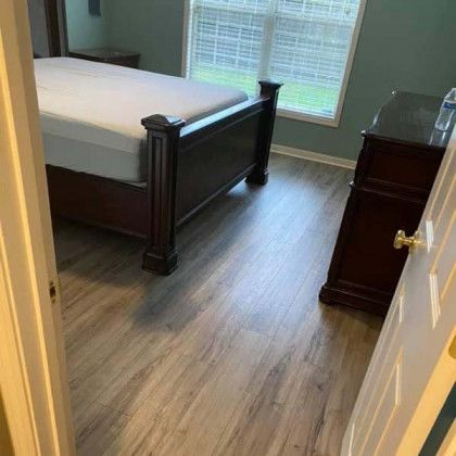 Bedroom with a dark wood bed, dresser, and gray wood-look flooring. Window in the background.