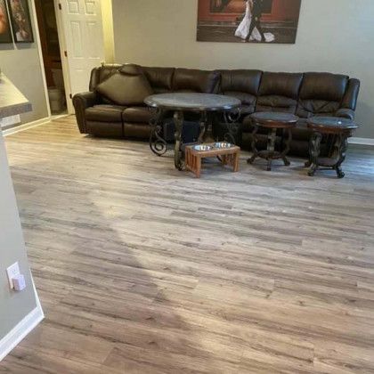 Living room with brown leather sectional, wooden tables, and laminate flooring.