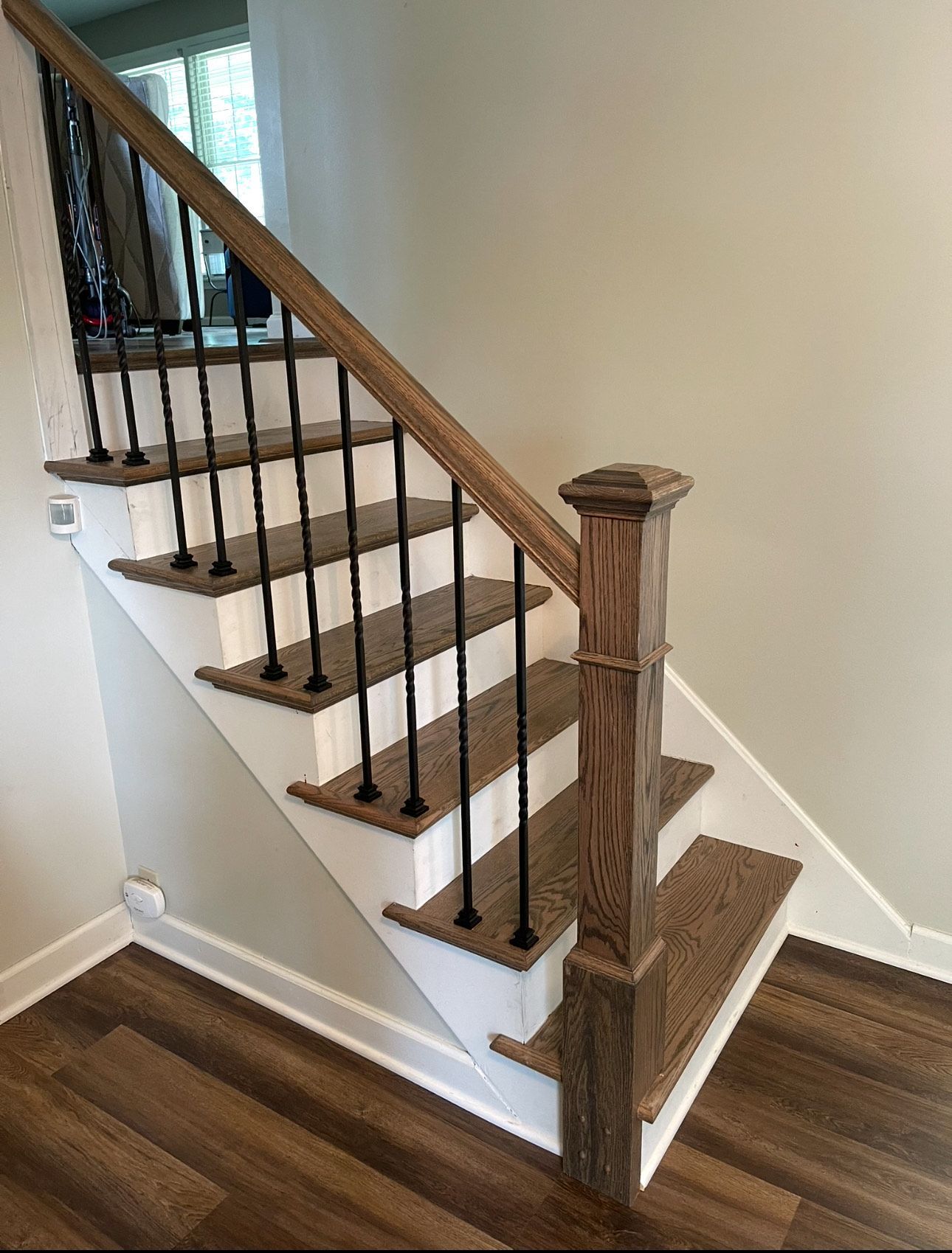 Staircase with brown treads, white risers, wooden railing, and black spindles.
