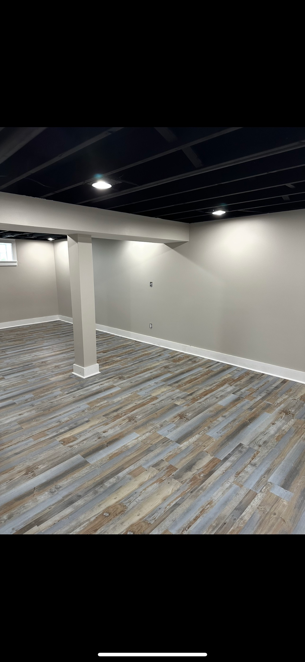 Finished basement with wood-look flooring, a black ceiling, and neutral-colored walls.