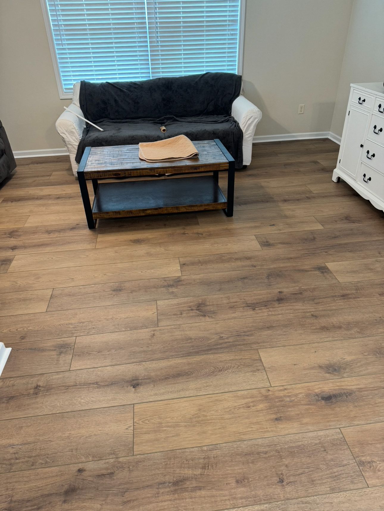 Living room with brown wood-look flooring, a white couch with black throw, and a dark coffee table.