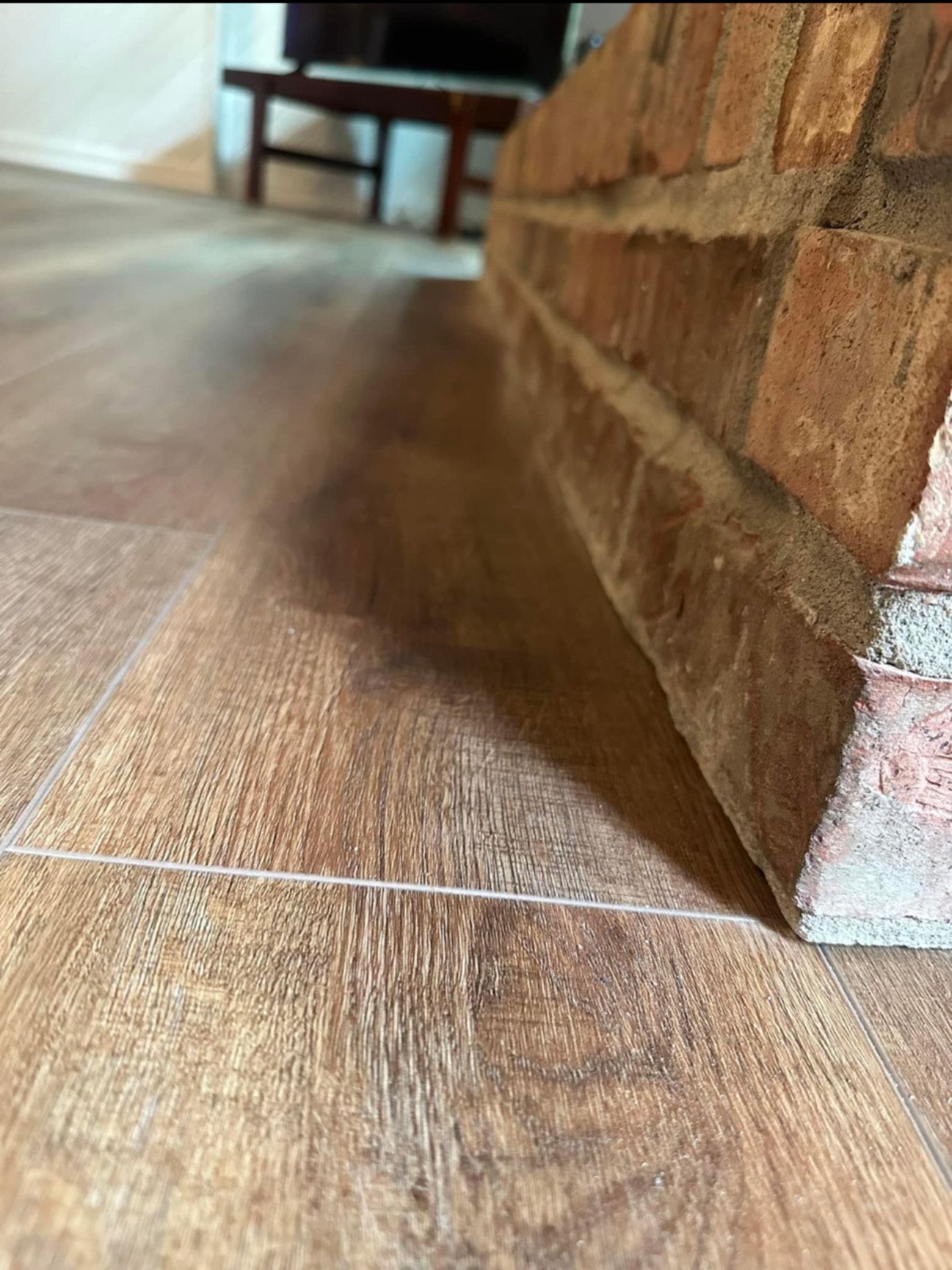 Wooden floor next to a red brick fireplace.
