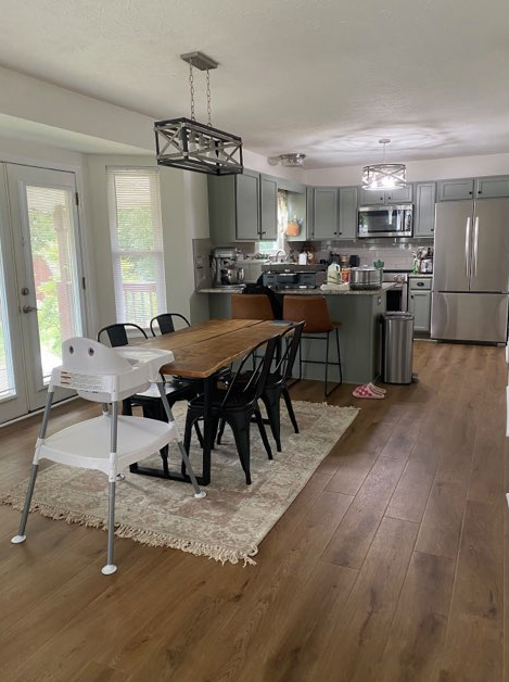 Kitchen with wooden floor, a table and chairs, light-colored cabinets, and stainless steel appliances.