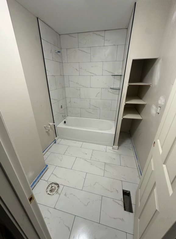 Newly renovated bathroom with white marble-look tiles, a bathtub, and built-in shelving.