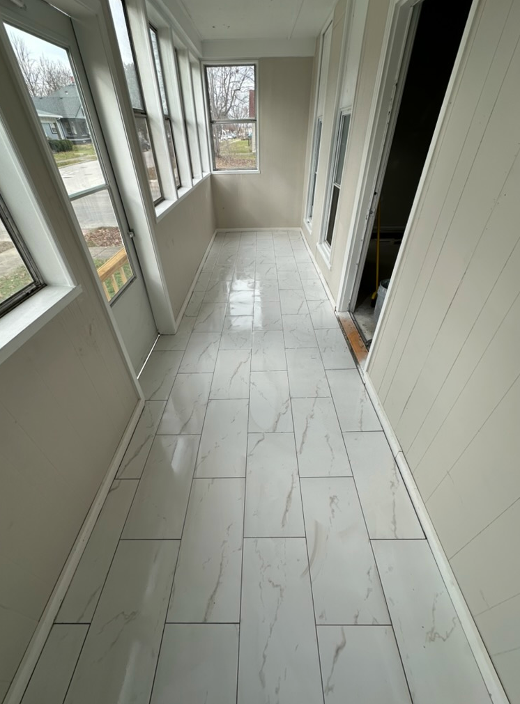 A narrow hallway with white tile flooring and windows on the left.