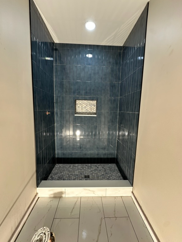 Walk-in shower with blue tile walls, pebble floor, and white step.