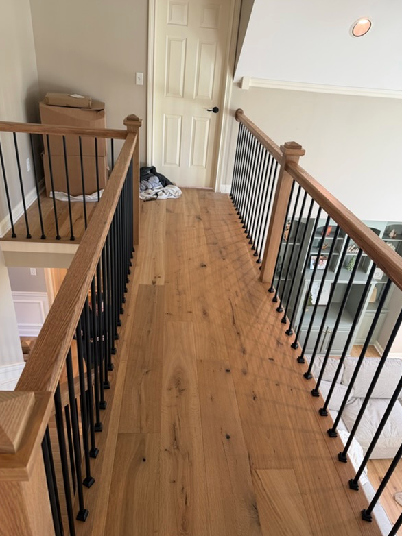 Wooden hallway with railing and black spindles, leading to a door.