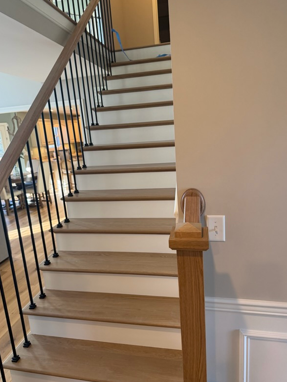 Wooden staircase with white risers, black metal balusters, and a wooden handrail.