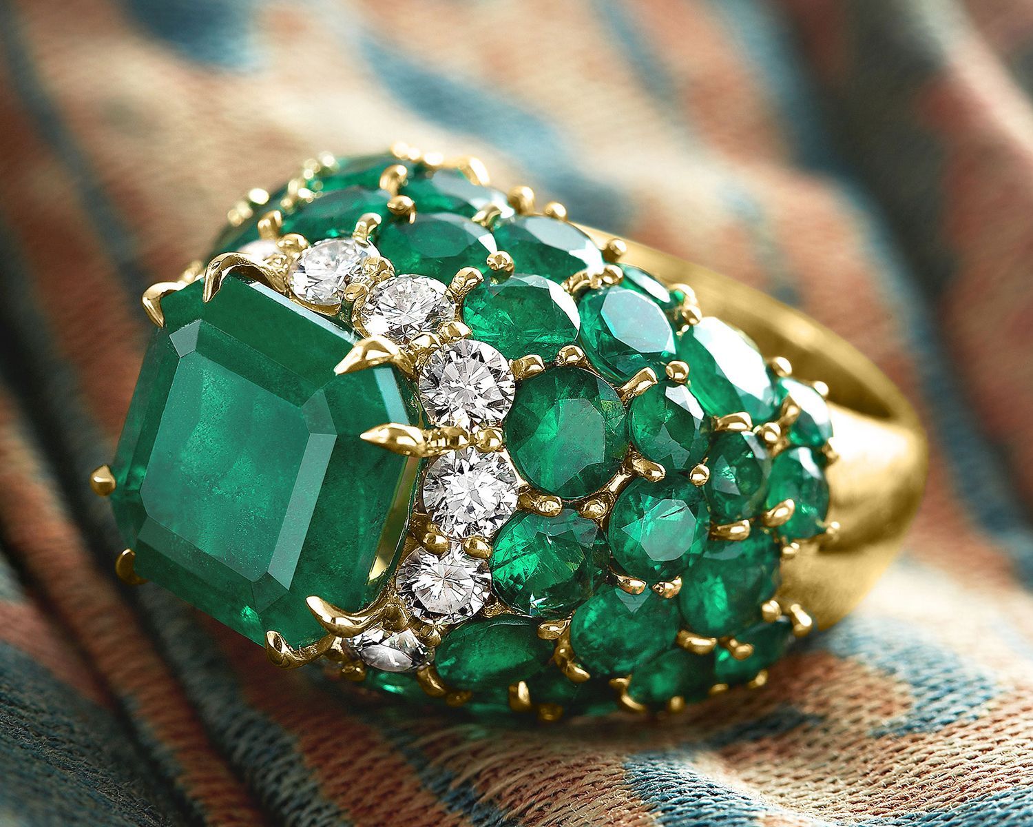 Gold ring with a large emerald center stone, surrounded by smaller emeralds and diamonds.