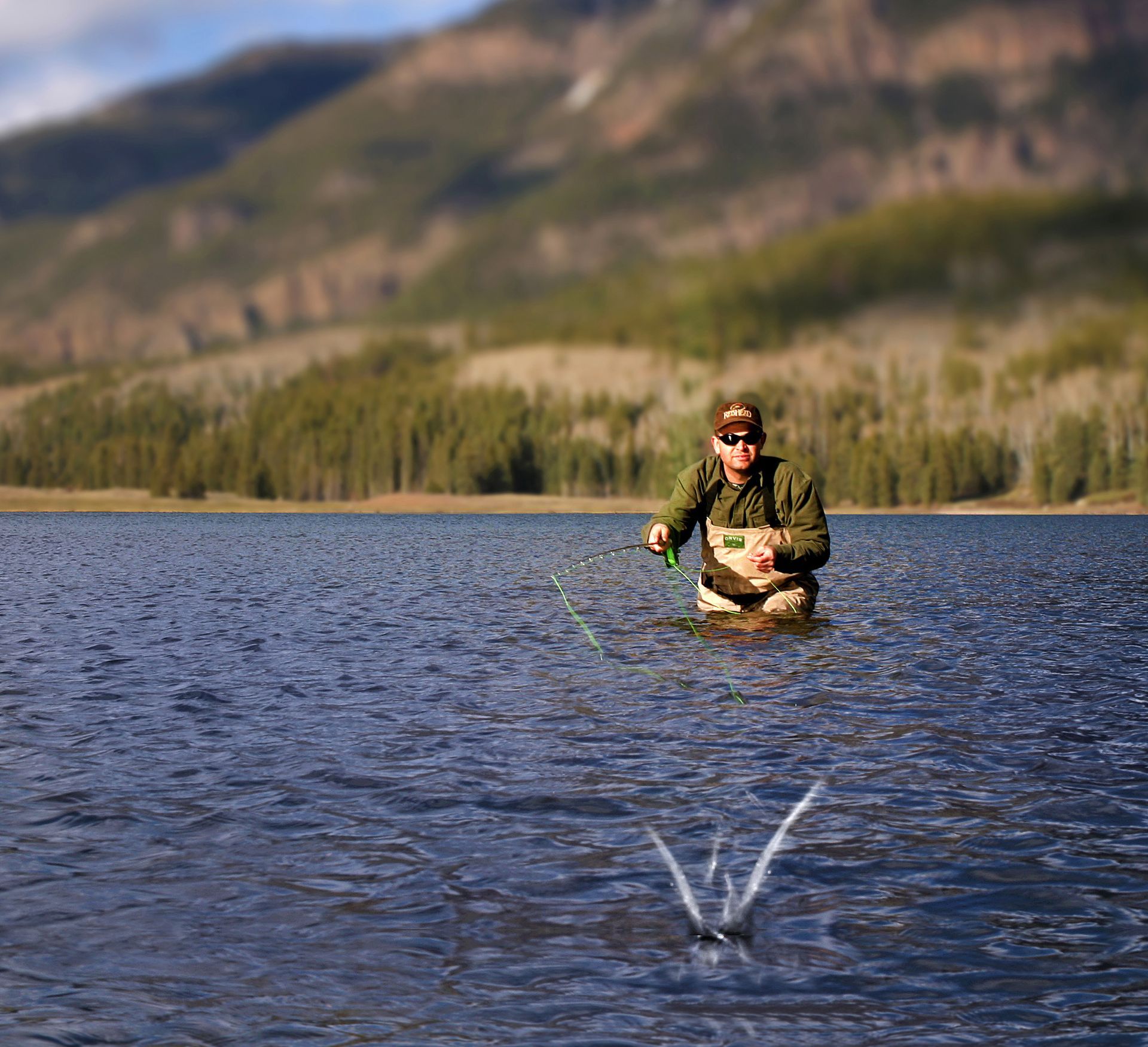 Man fly fishing in a lake, mountains in the background.