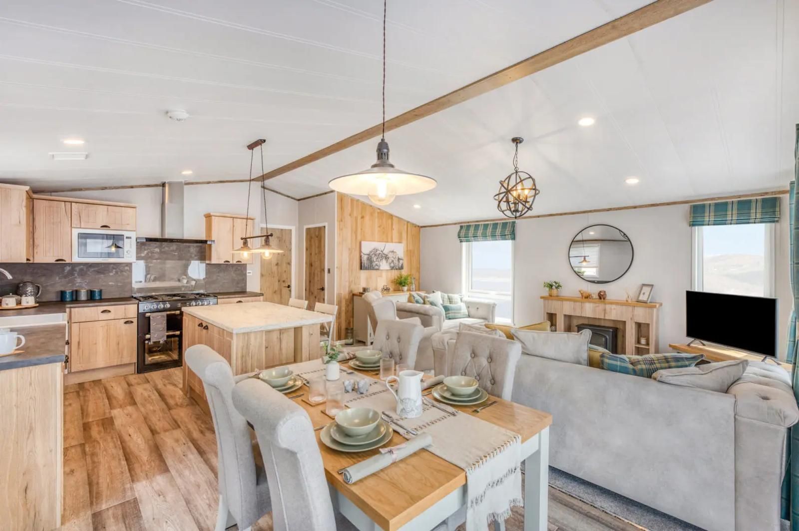 A bright, modern open-plan kitchen, dining area, and living room with light wood cabinets, seating, and neutral decor.