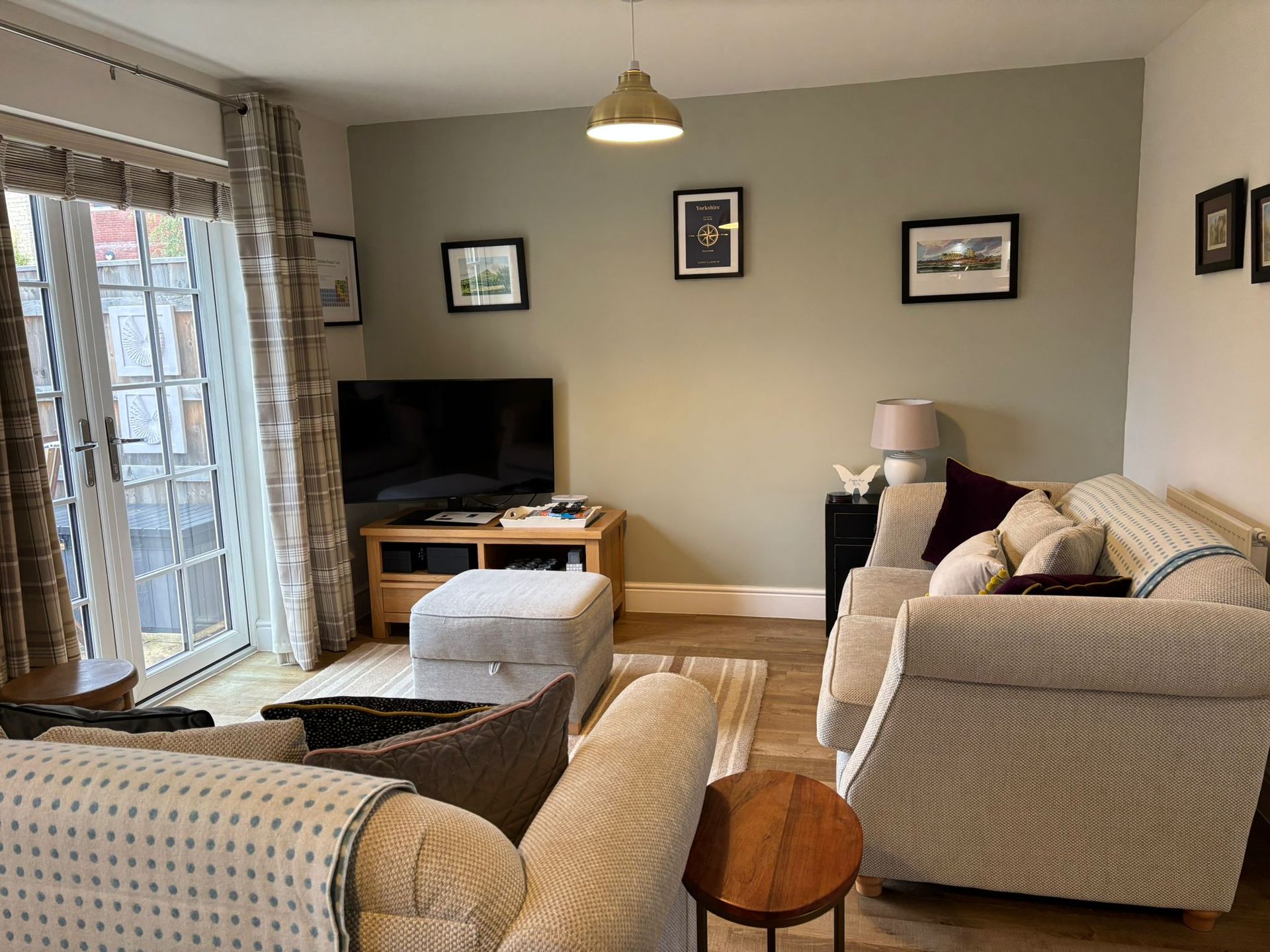 A cozy living room with a light green accent wall, two fabric sofas, a TV on a wooden stand, and glass patio doors.