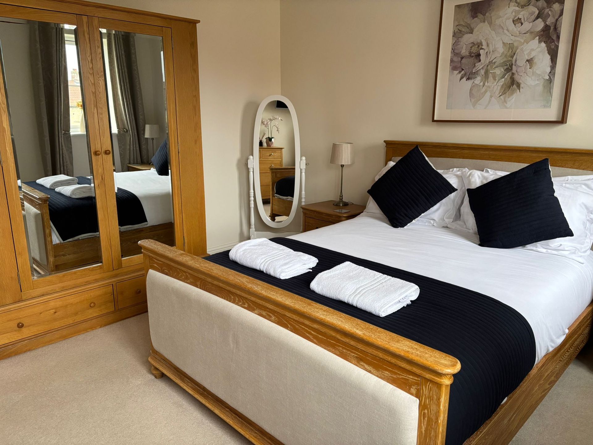 A bedroom featuring a wooden bed with a black runner and pillows, a matching wardrobe with a mirror, and wall art.