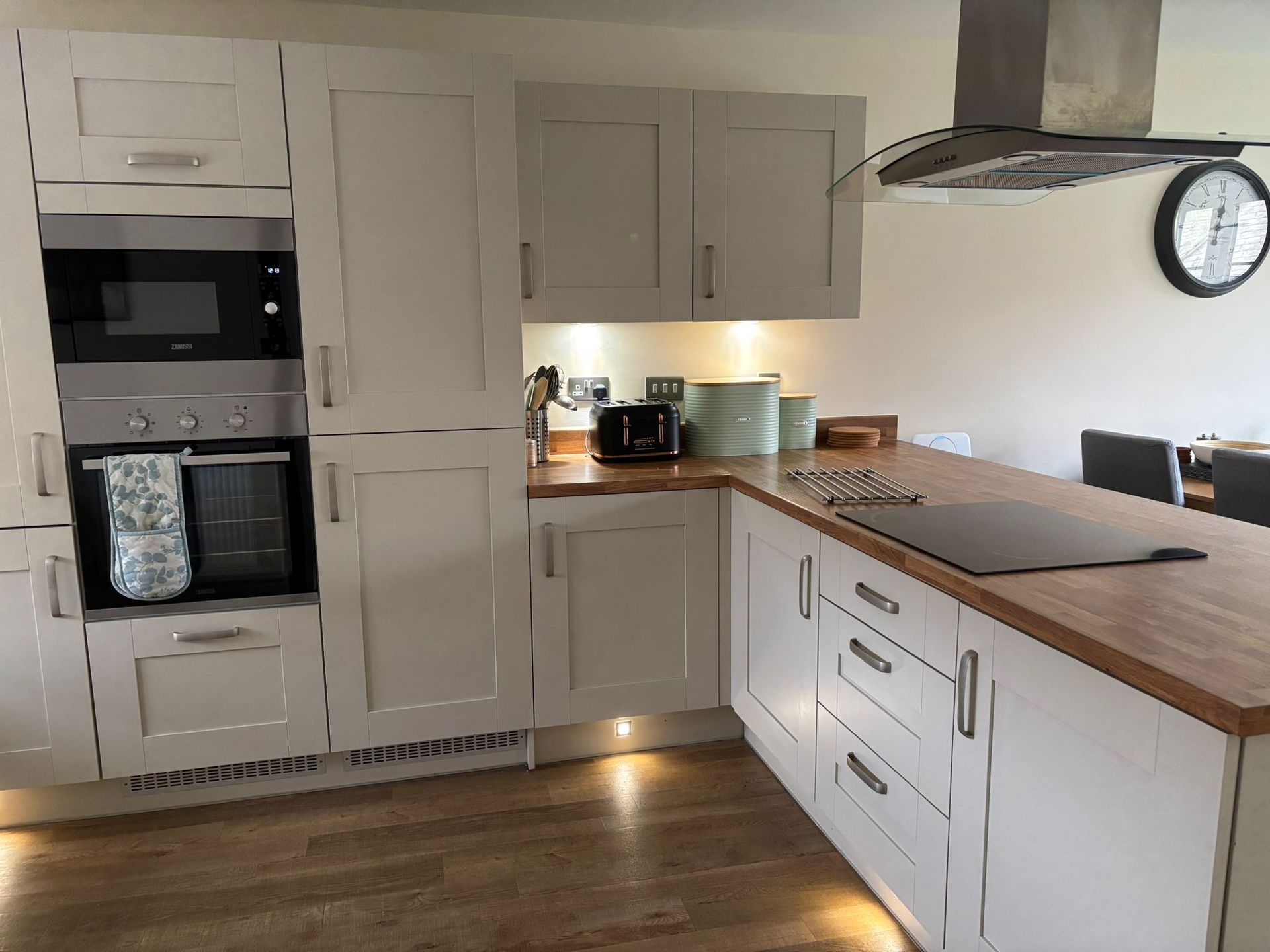 Modern kitchen with light cream cabinets, wood countertops, stainless steel appliances, and a wall clock.