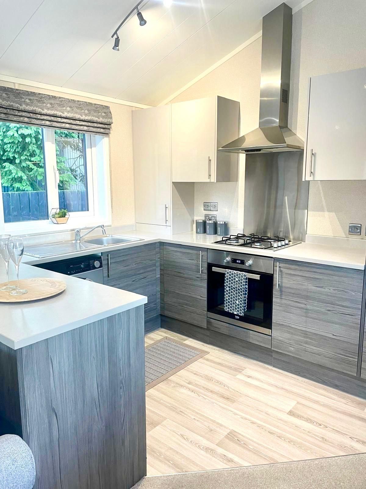 A modern kitchen with grey wood-grain cabinets, white countertops, stainless steel appliances, and wood-look flooring.