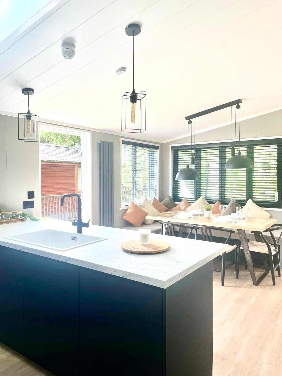 Modern kitchen interior featuring a black island with a sink, pendant lighting, and a dining area with window shutters.