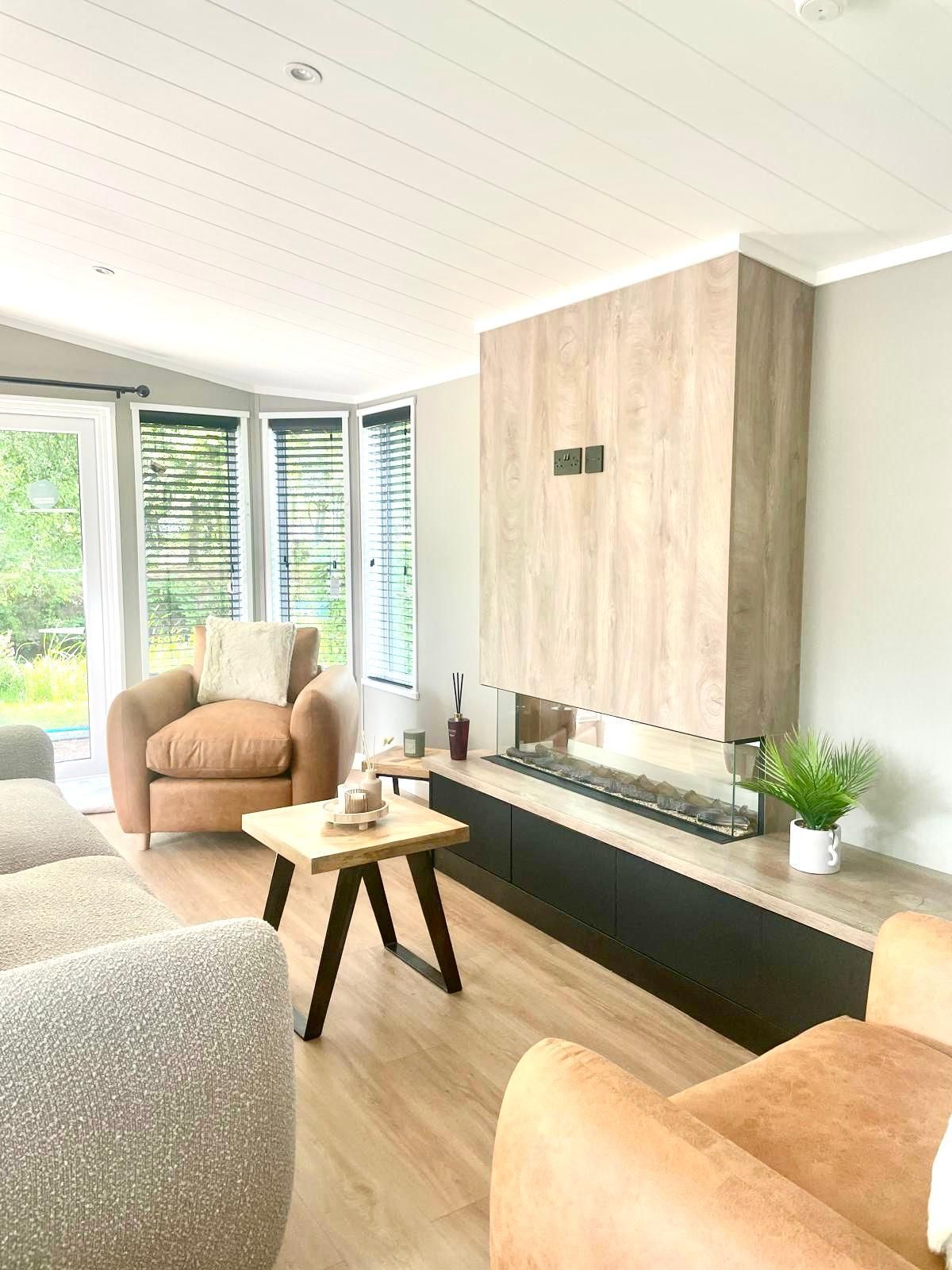 A modern living room with leather armchairs, a wooden coffee table, and a linear fireplace built into a wood-paneled wall.