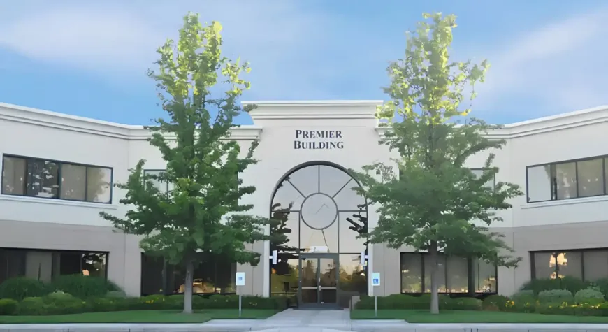 Modern office building entrance with a large circular clock and tall trees in front