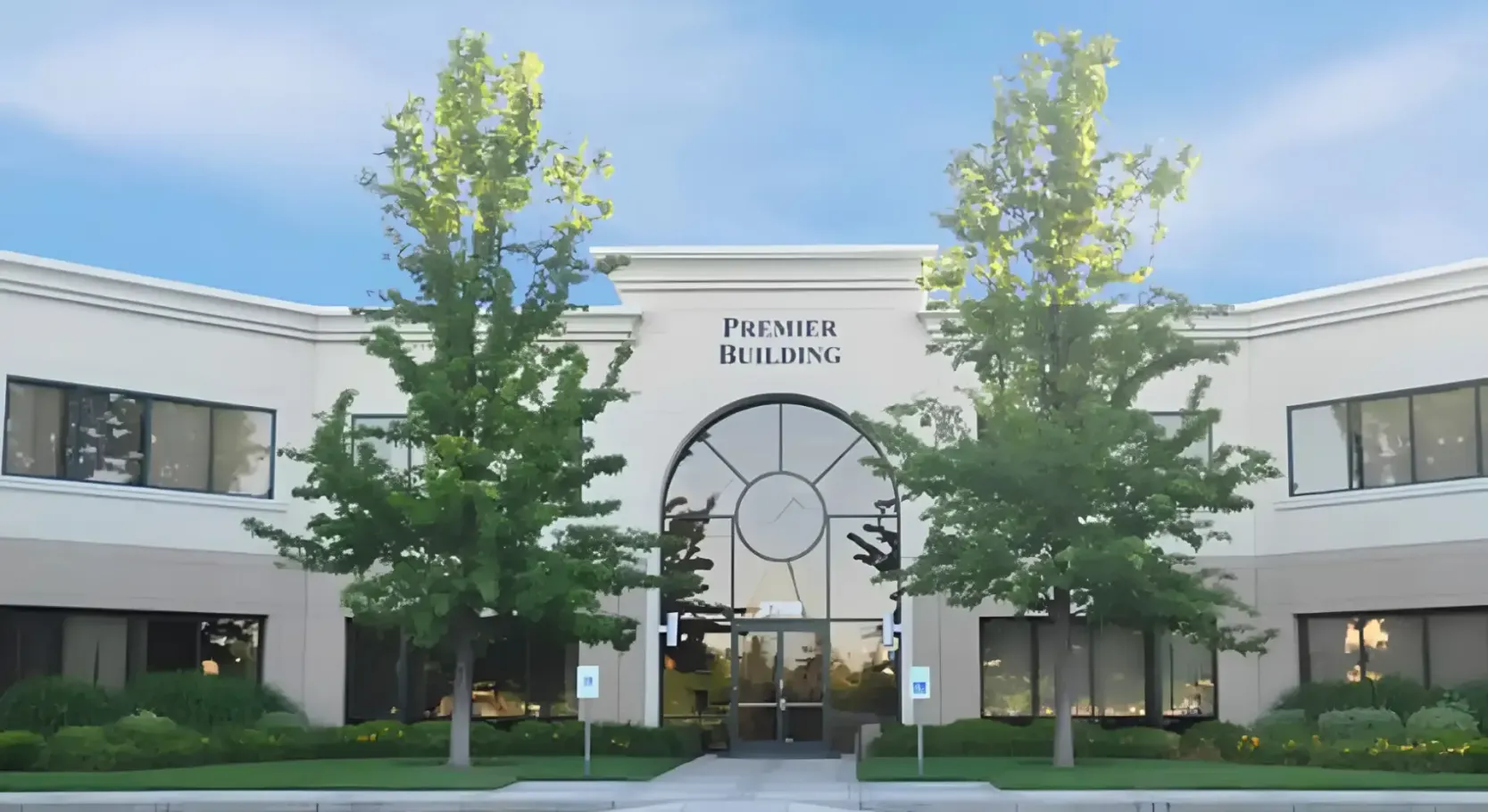 Office building with arched entrance and two trees in front, under a bright blue sky