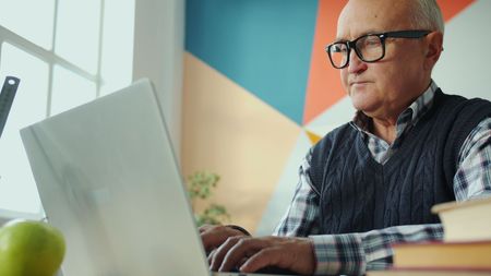 Man typing on a laptop at a desk, with a geometric wall backdrop and a green apple nearby