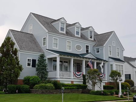 Large gray Victorian-style house with white trim and American flags, viewed from the front yard