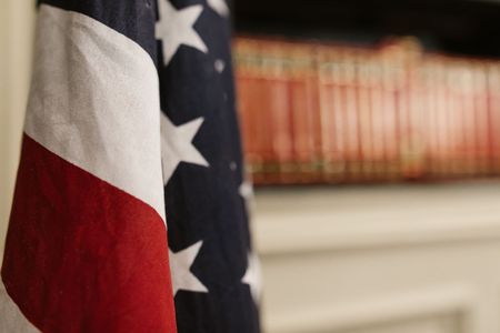 Close-up of an American flag with stars and red-and-white stripes in front of blurred bookshelves