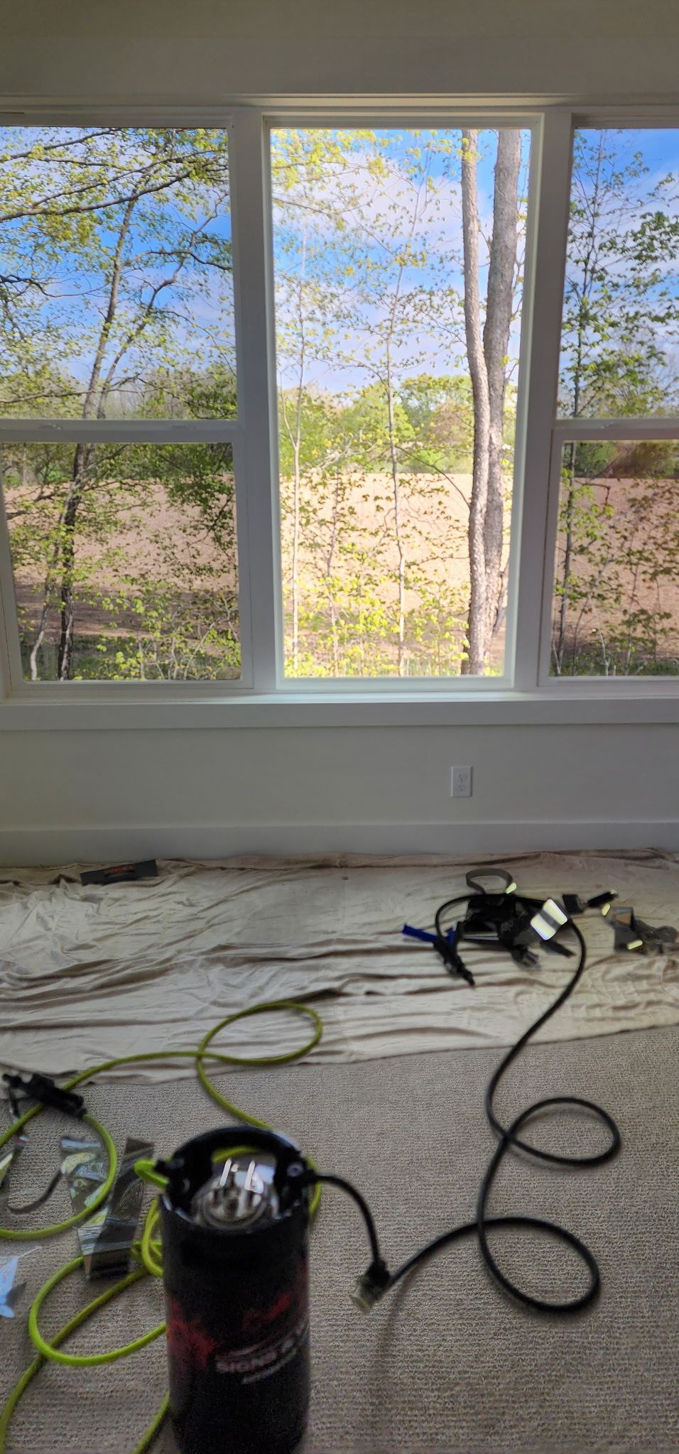 Bright room with large windows, a bare floor, and cords and tools scattered in the foreground