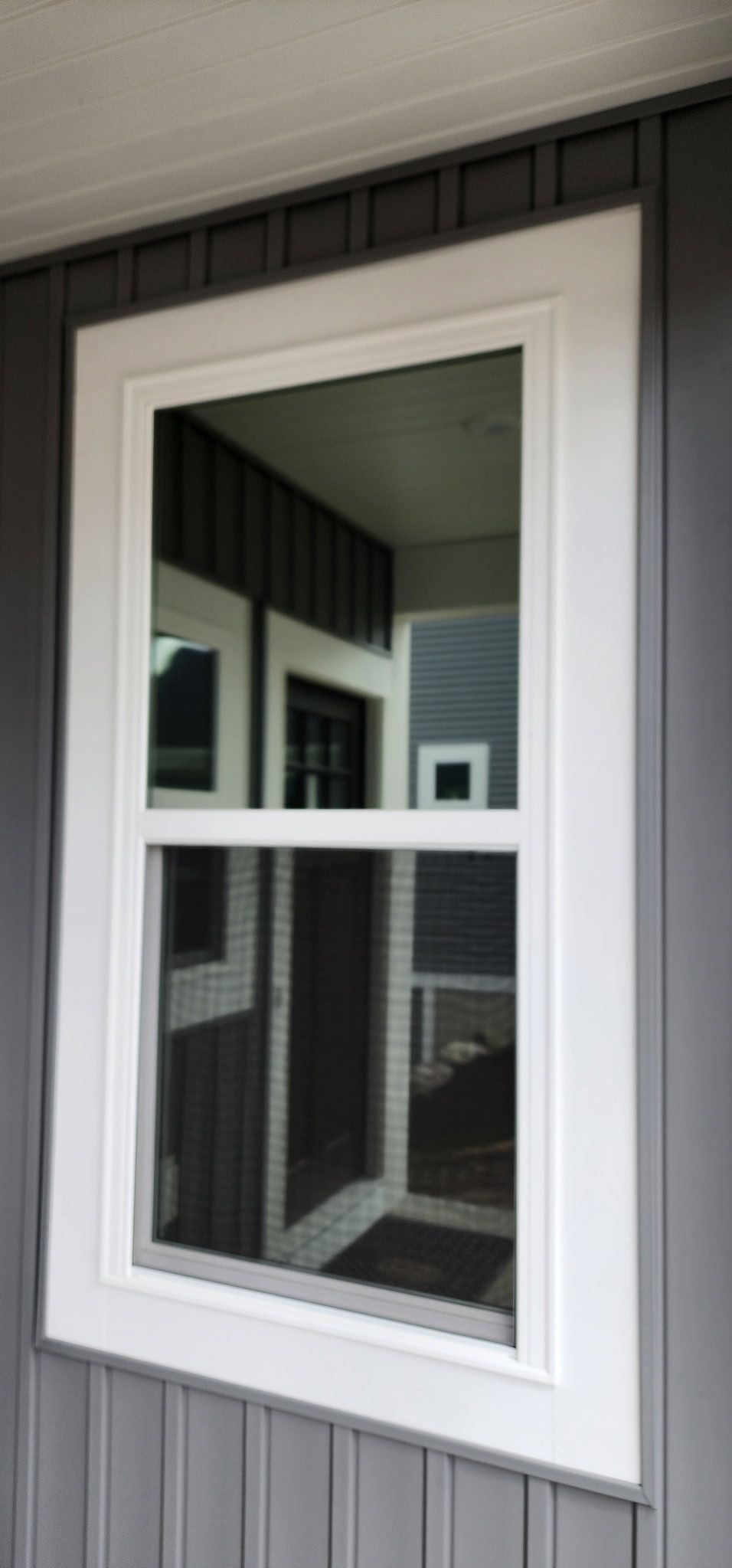 White-framed window on a gray house exterior, reflecting nearby porch and siding.