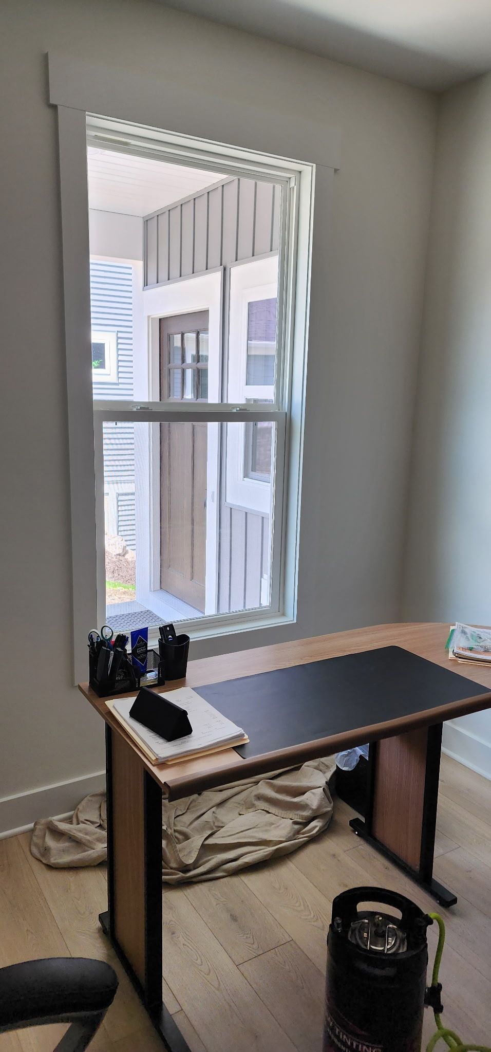 Small home office by a window with a standing desk, monitor, chair, and cords on the floor.
