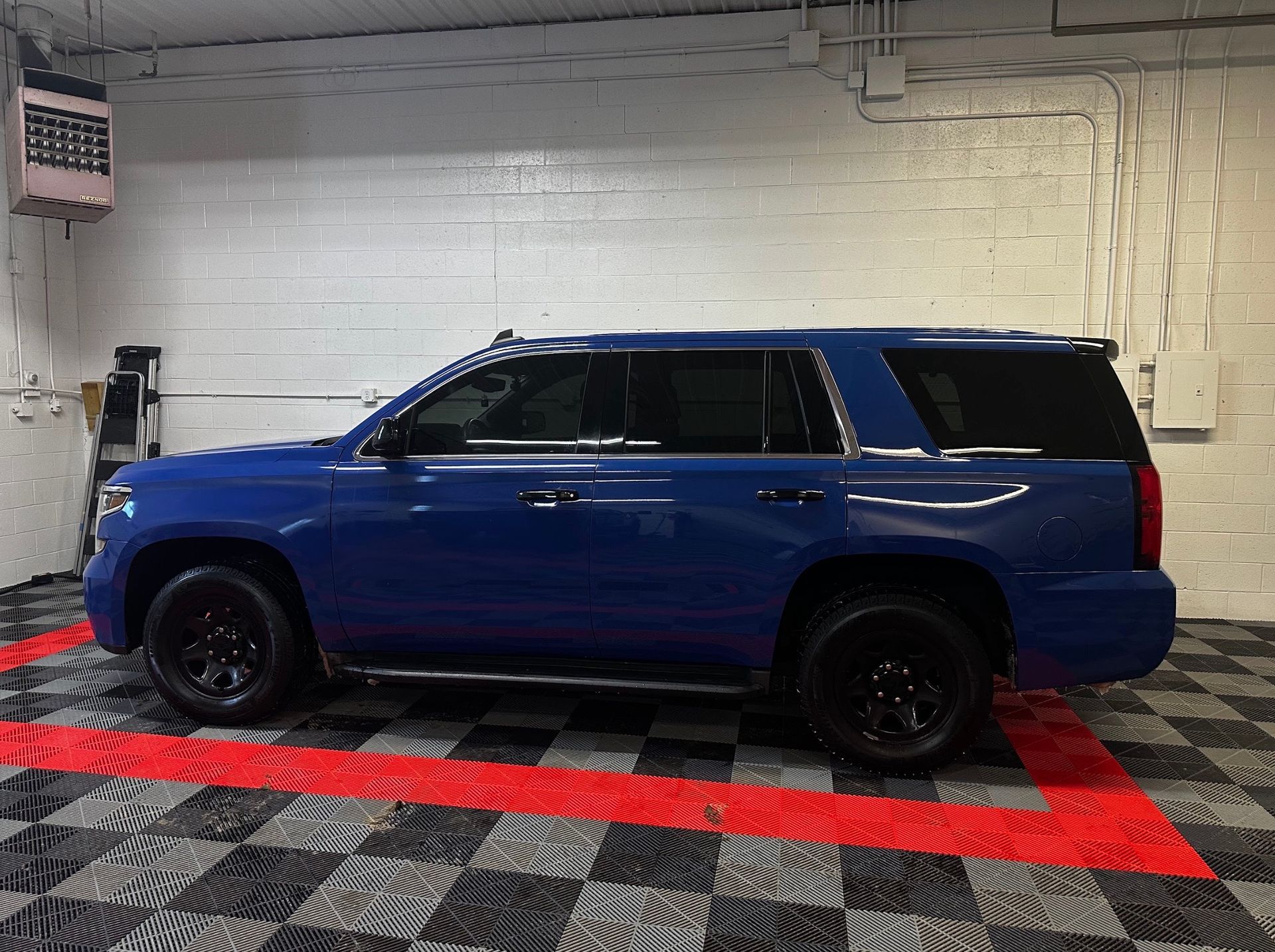 Blue SUV parked indoors on a red-and-black checkered floor against a white brick wall.