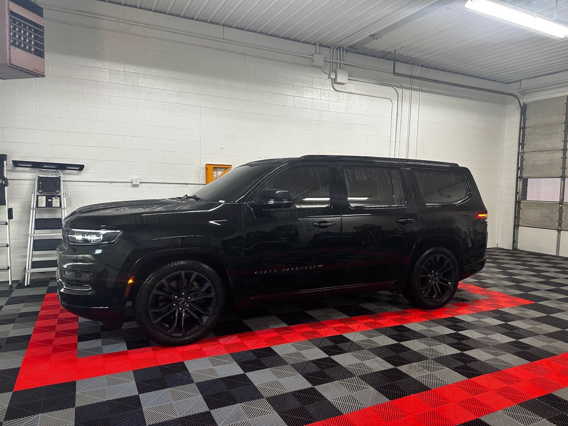 Black SUV parked indoors on a red and black checkered floor in a garage.