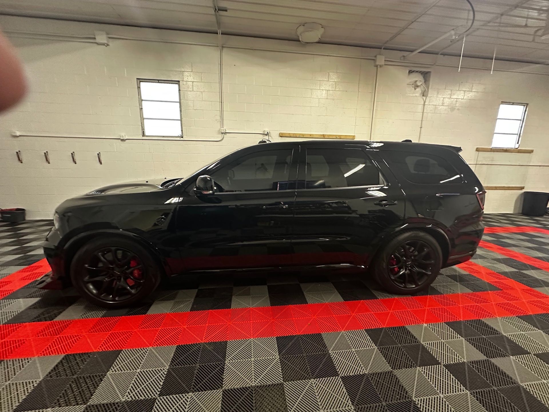 Black SUV in a garage with red floor markings, viewed from the side.