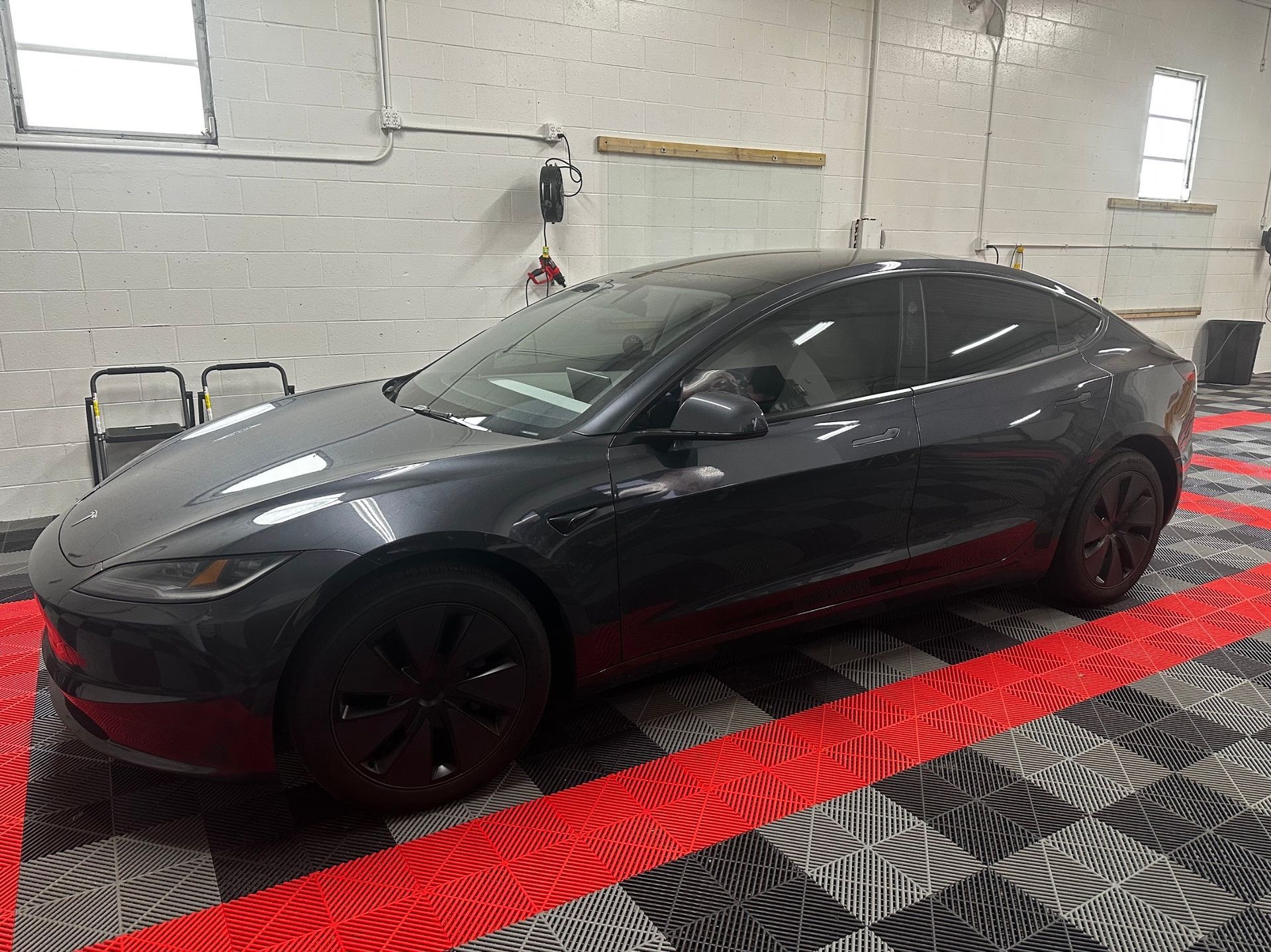 Dark gray sedan in a garage on a red and black patterned floor mat.