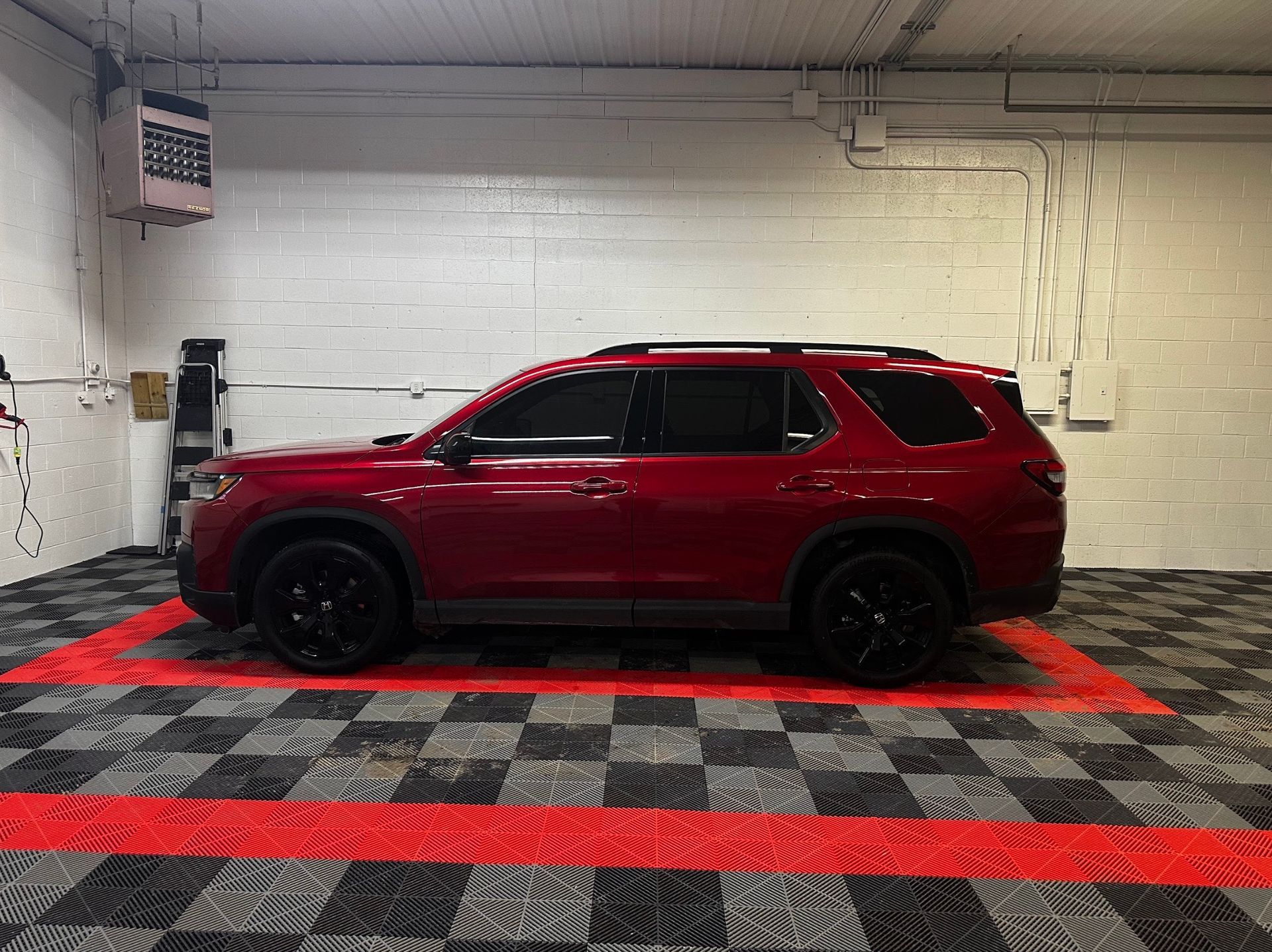 Red SUV parked in an indoor garage with white brick walls and red floor markings.