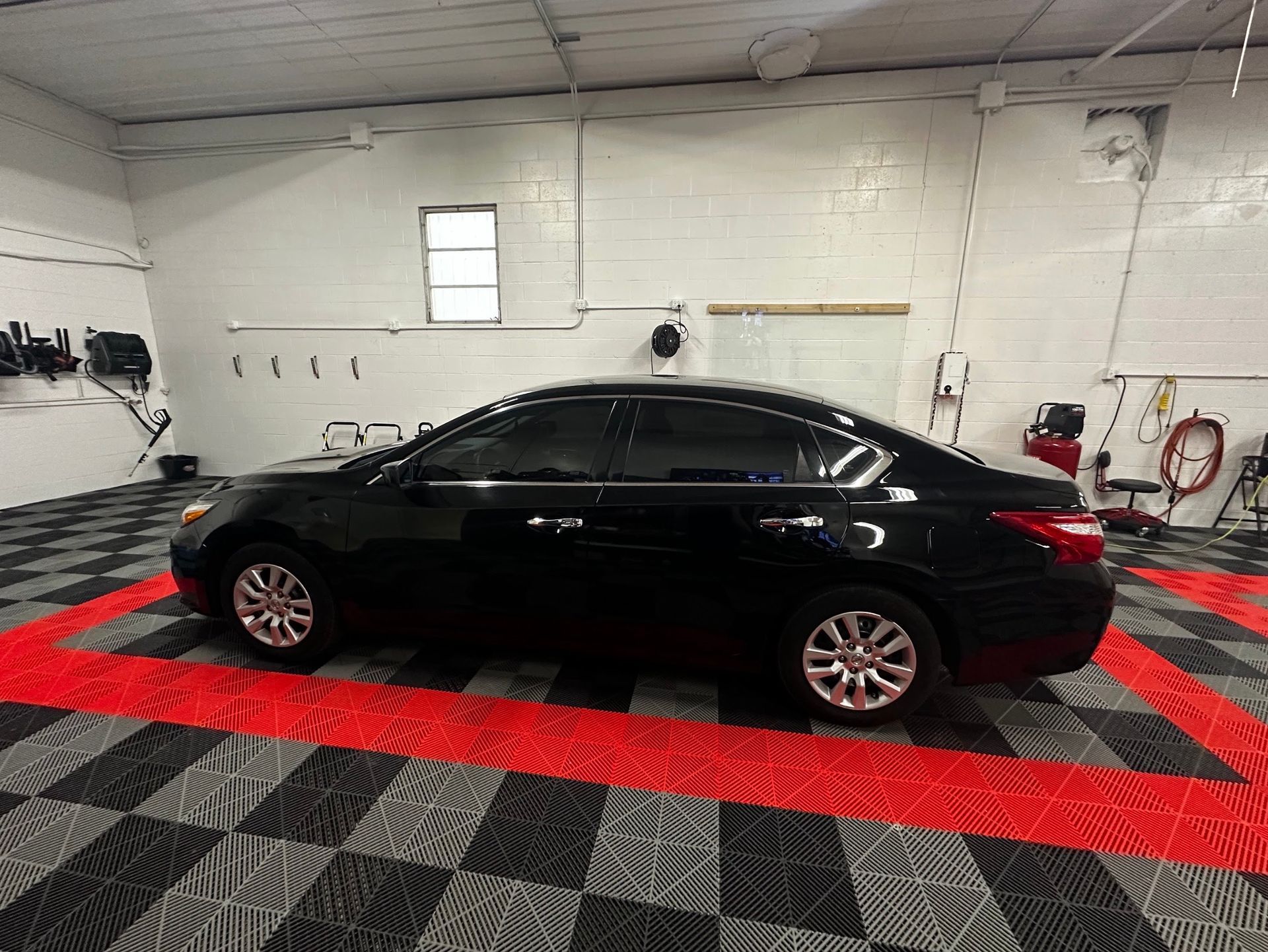Black sedan parked in a white garage on a red-and-black checkered floor.