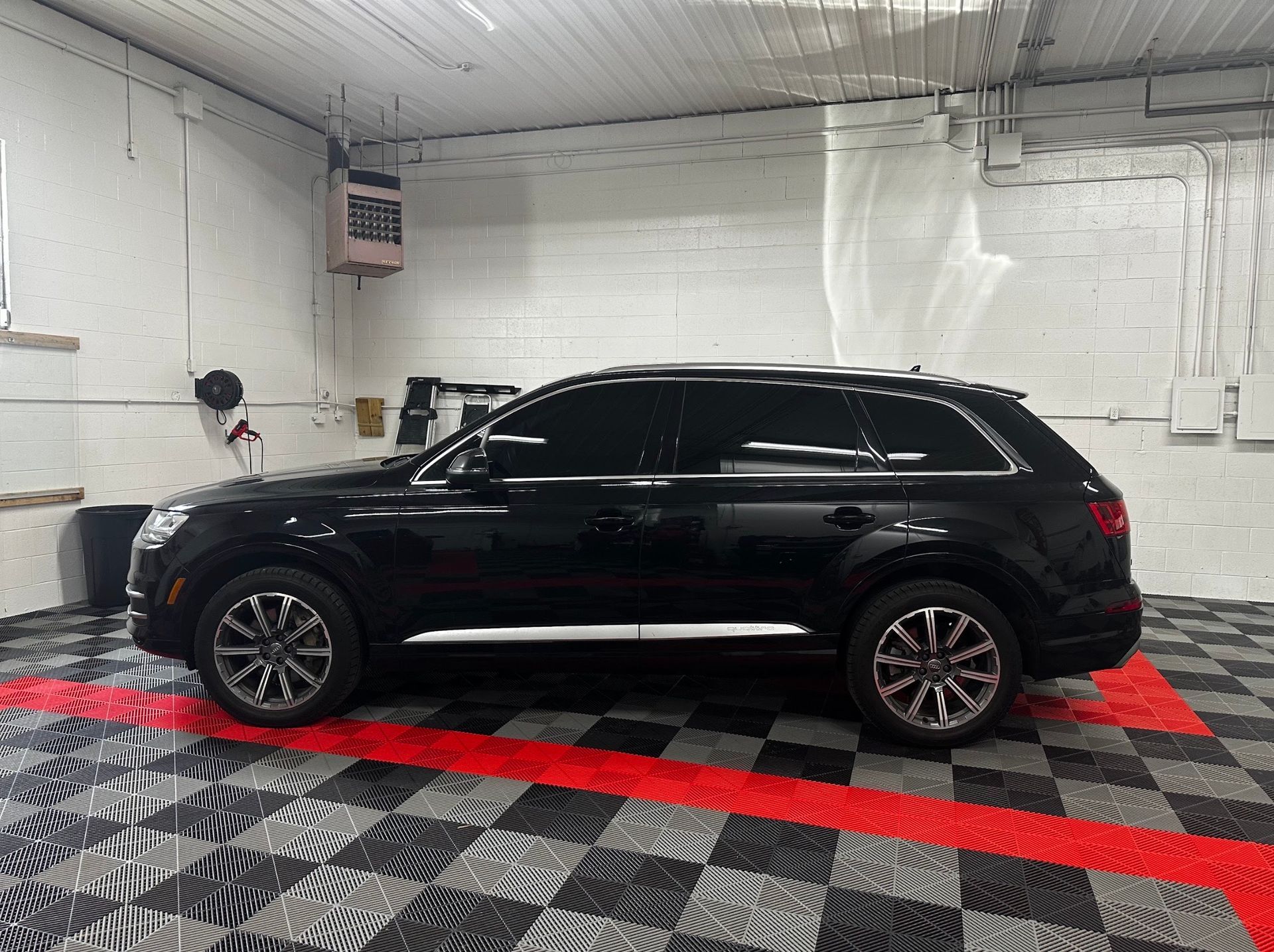 Black SUV parked indoors on a red mat in a bright garage or detailing bay.