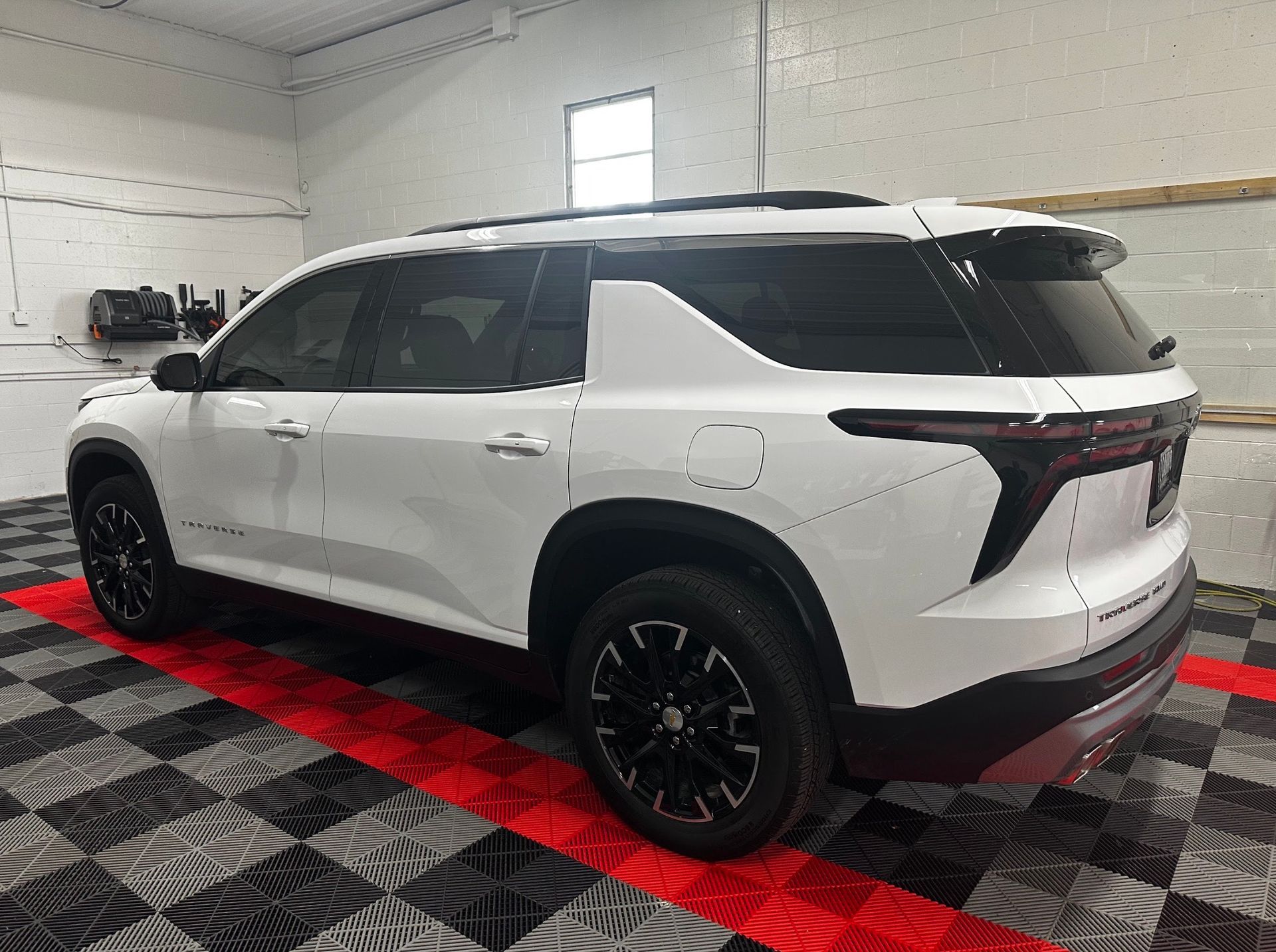 White SUV with black wheels parked indoors on a red and black checkered floor.