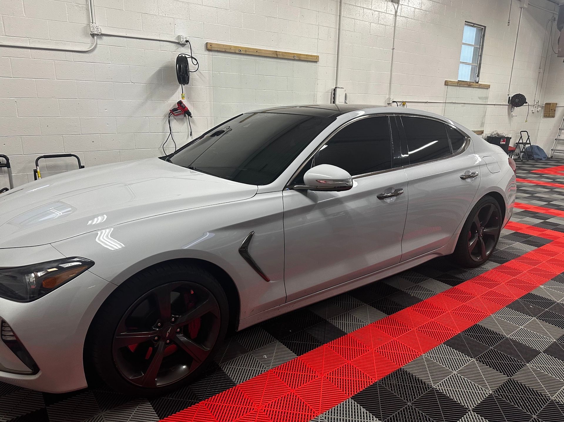 Silver sports coupe parked indoors on a red-and-black floor mat, viewed from the side.