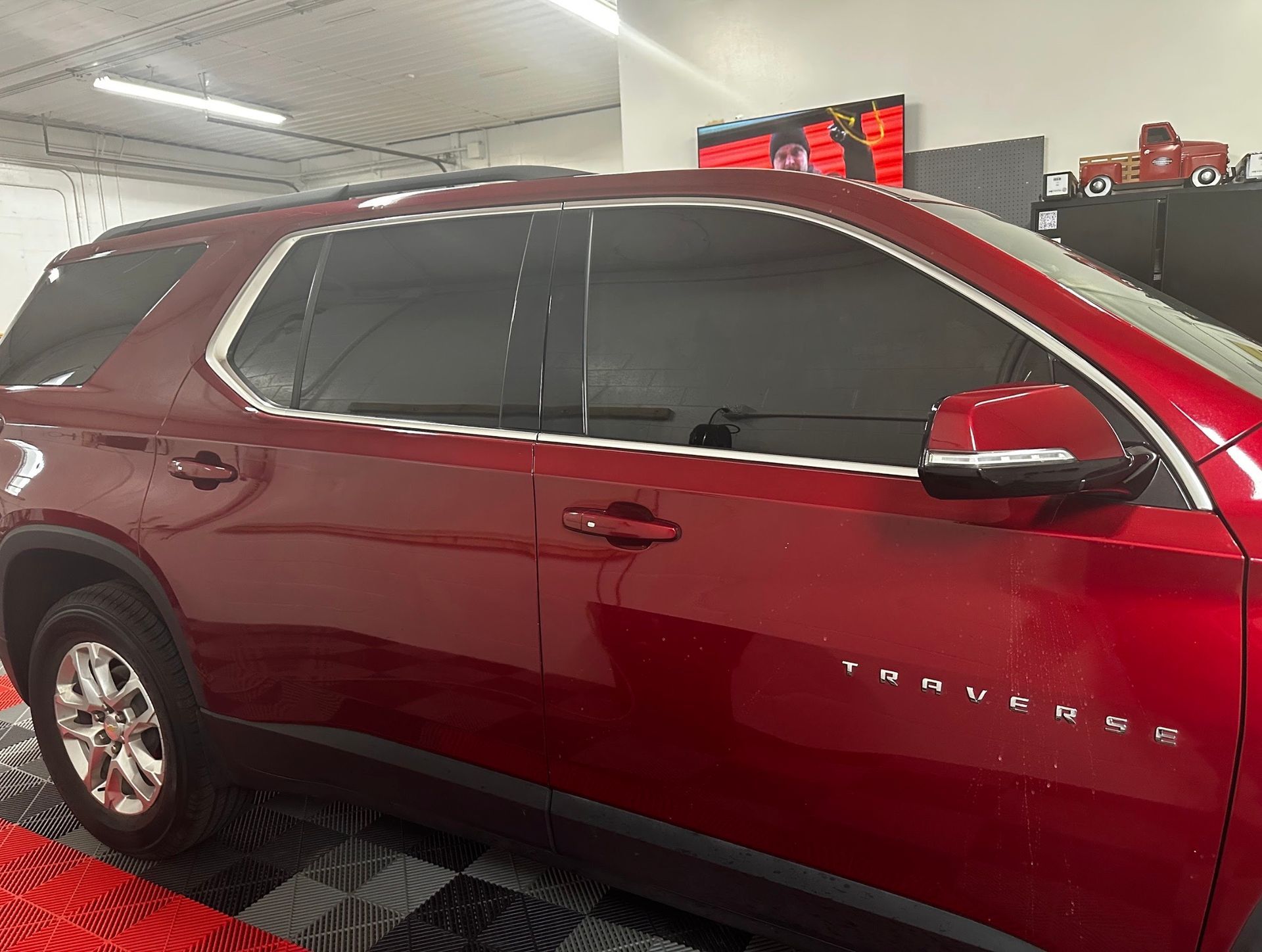 Red Chevrolet Traverse SUV in a showroom, side view with tinted windows and red paint.